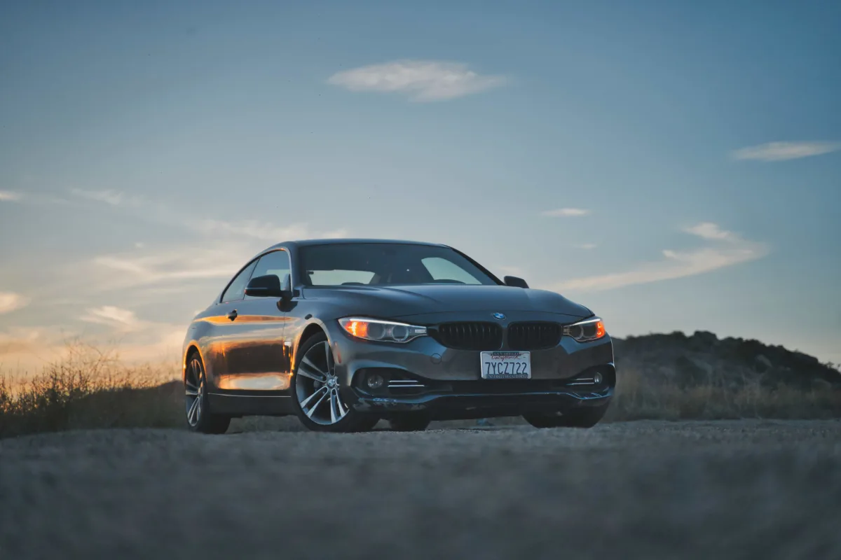 A grey BMW coupe parked on a dirt ridge against a sunset sky