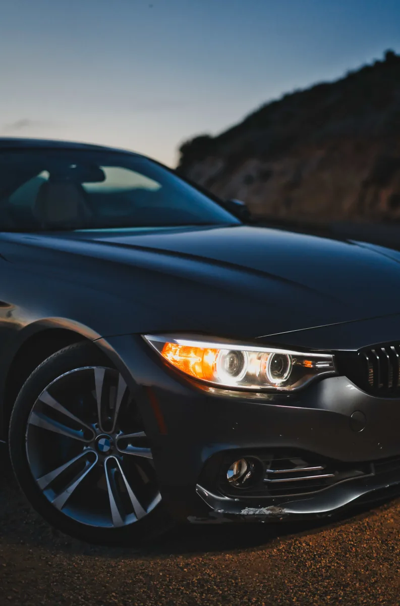 Close detail of a grey BMW coupe's headlight and front wheel at dusk