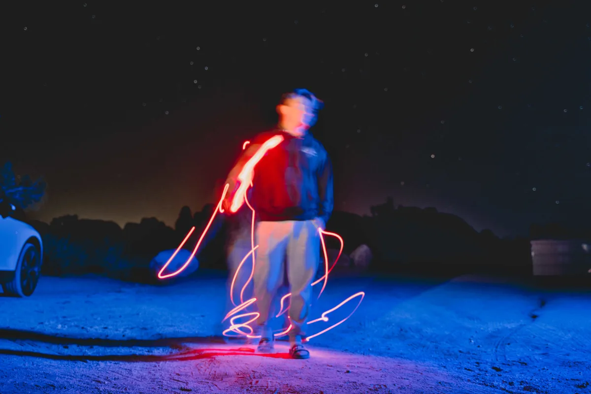 Long-exposure light painting at night, red loops of light drawn around a blurred standing figure