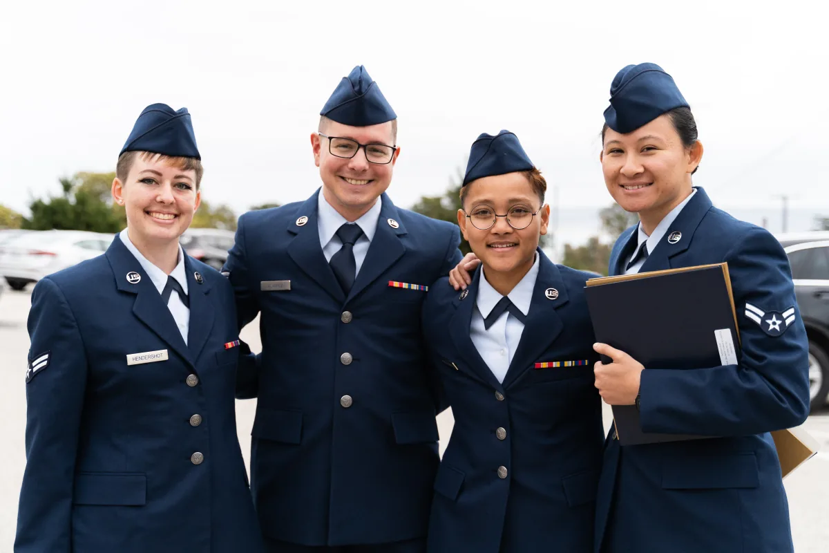 Four airmen in dress blues stand shoulder to shoulder, smiling at the camera