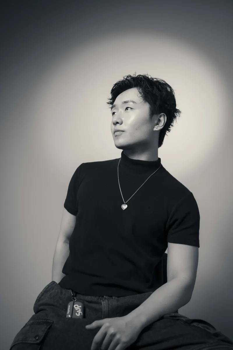 Black and white studio portrait, curly hair and a heart pendant, looking up and away from the camera