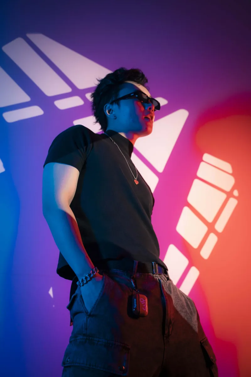Low-angle portrait in sunglasses against a wall washed in red and blue neon