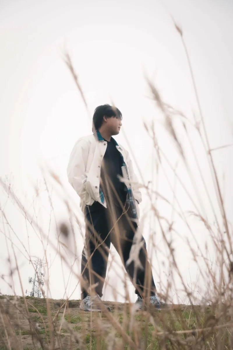 A figure in a white jacket on a ridge, seen through a blur of dry grass in the foreground