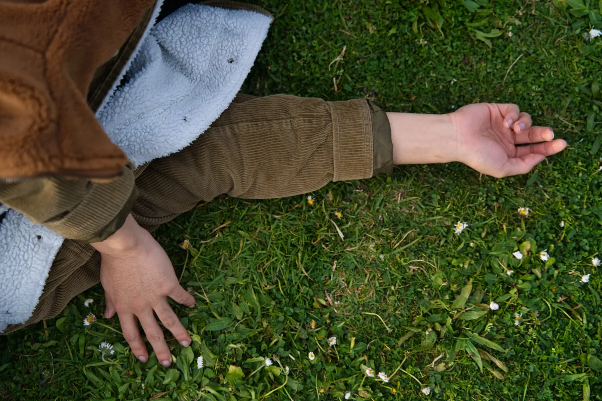 Overhead view of someone lying face down on grass scattered with daisies, arms outstretched